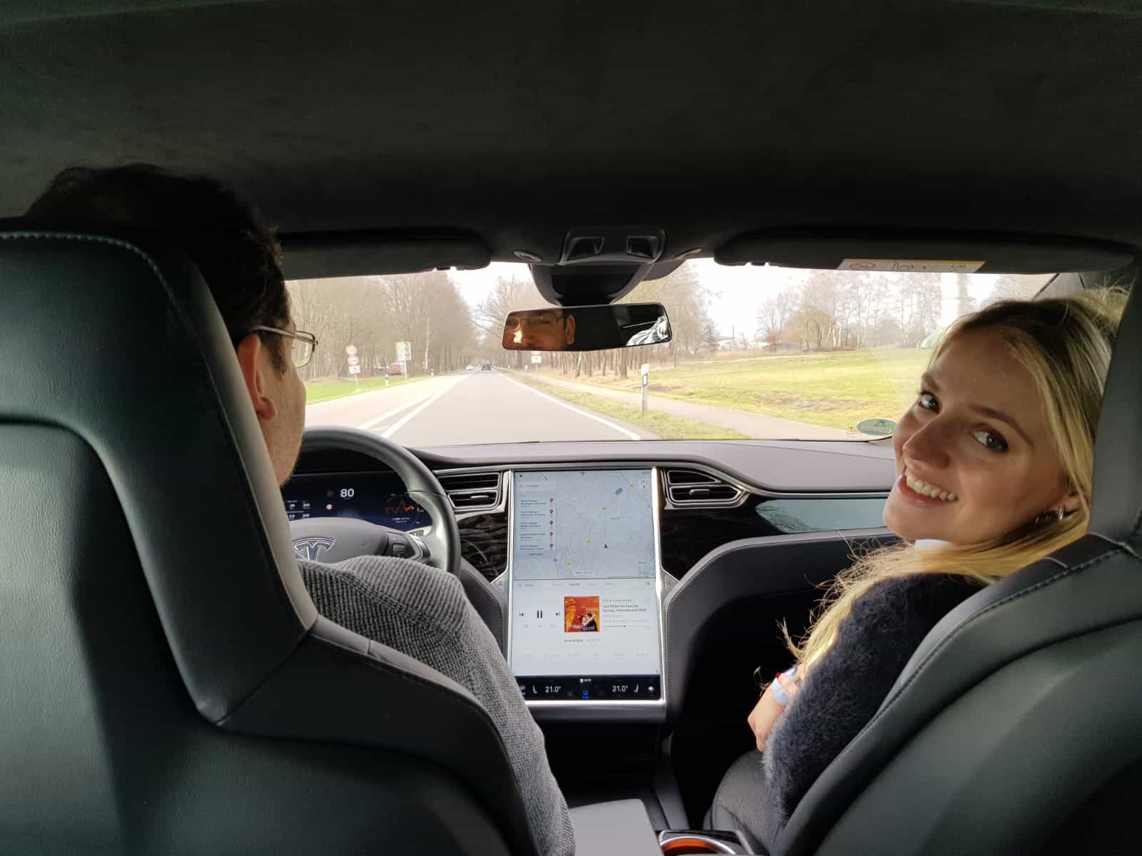viagem alemanha carros elétricos tesla transfers áustria suíça Casal no banco da frente de um carro, o homem ao volante e a mulher ao seu lado, ambos sorrindo.