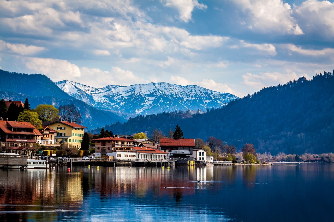 Lago Tegernsee na Baviera, com casas à beira da água e montanhas majestosas ao fundo.