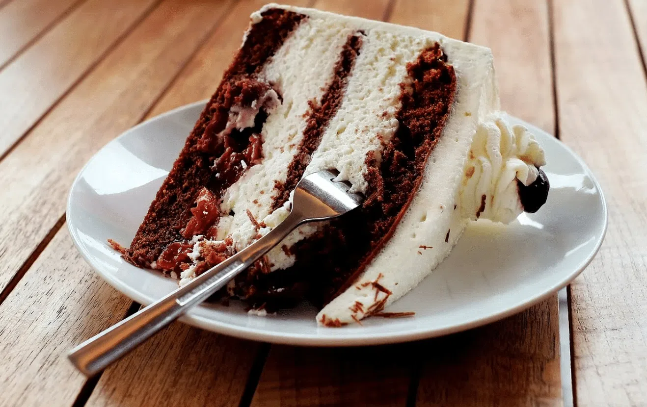 Fatia de bolo Floresta Negra com camadas de chocolate, creme e cerejas em um prato sobre mesa de madeira