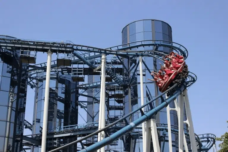 Montanha-russa vermelha descendo trilhos azuis no Europa-Park, com prédio de vidro ao fundo