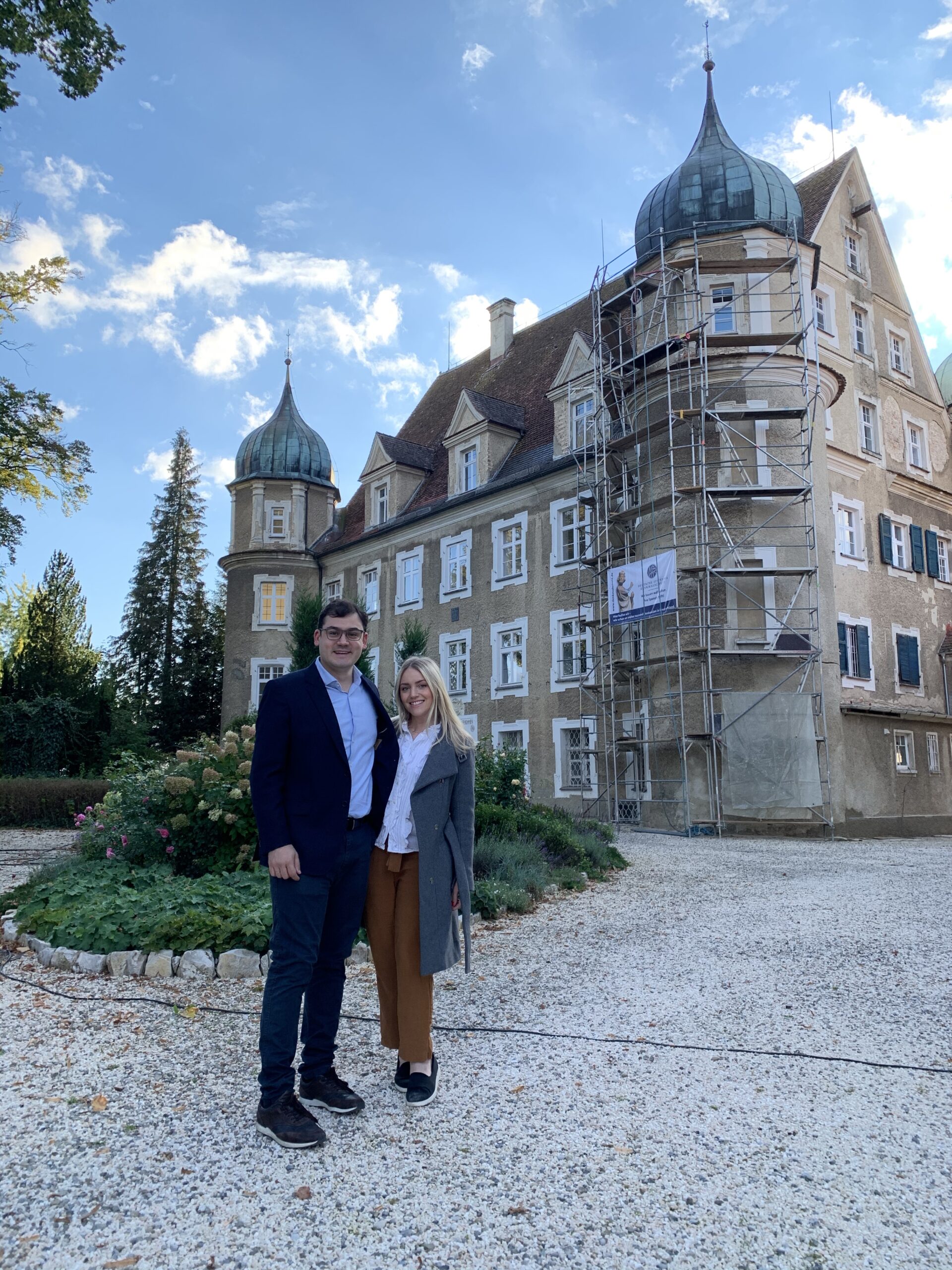 viagem-alemanha-palacio Casal em pé diante de um grande castelo, sorrindo e admirando a arquitetura.