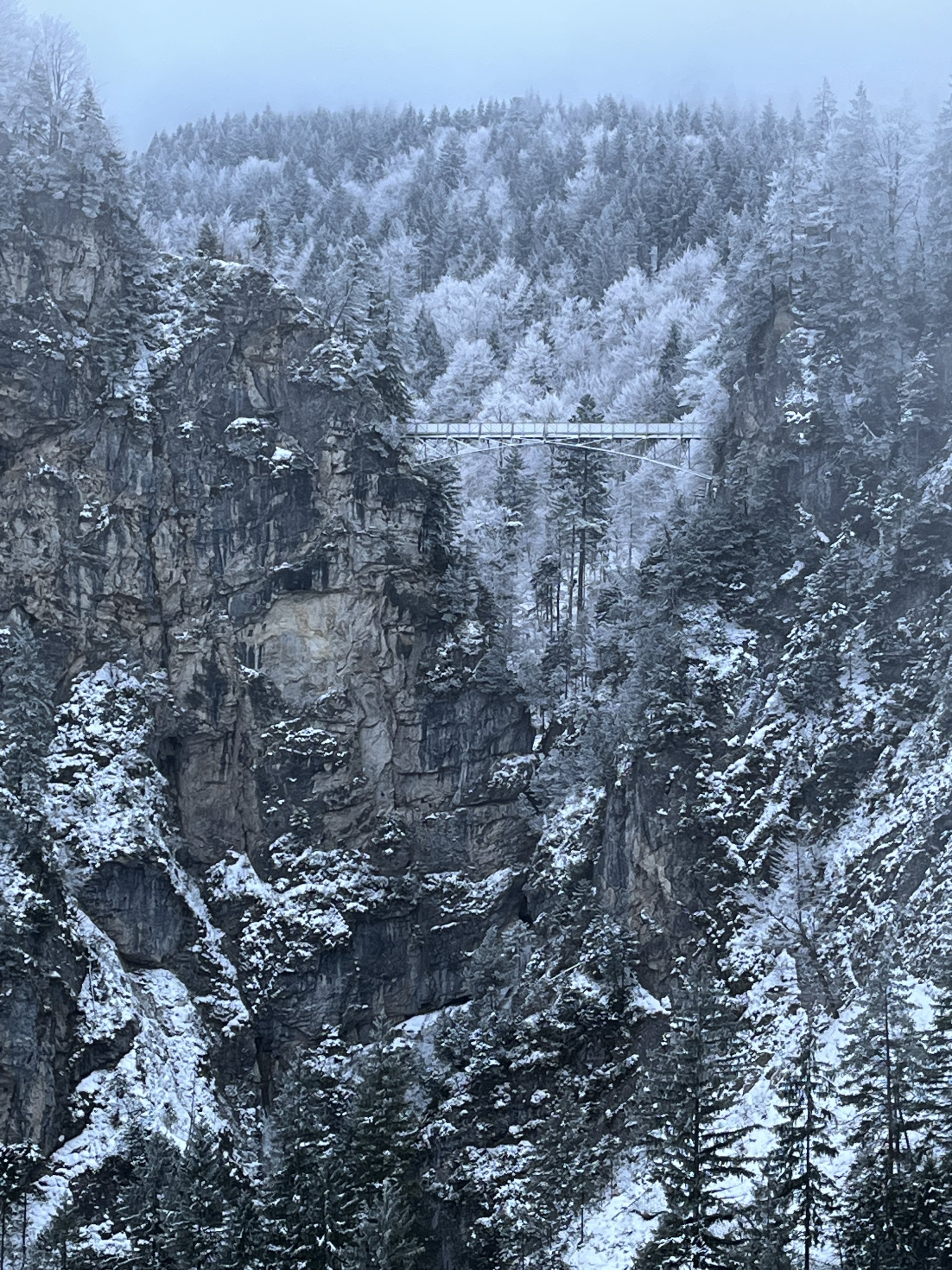Vista do Castelo de Neuschwanstein a partir da ponte Marienbrücke, enquadrado pelas montanhas dos Alpes.