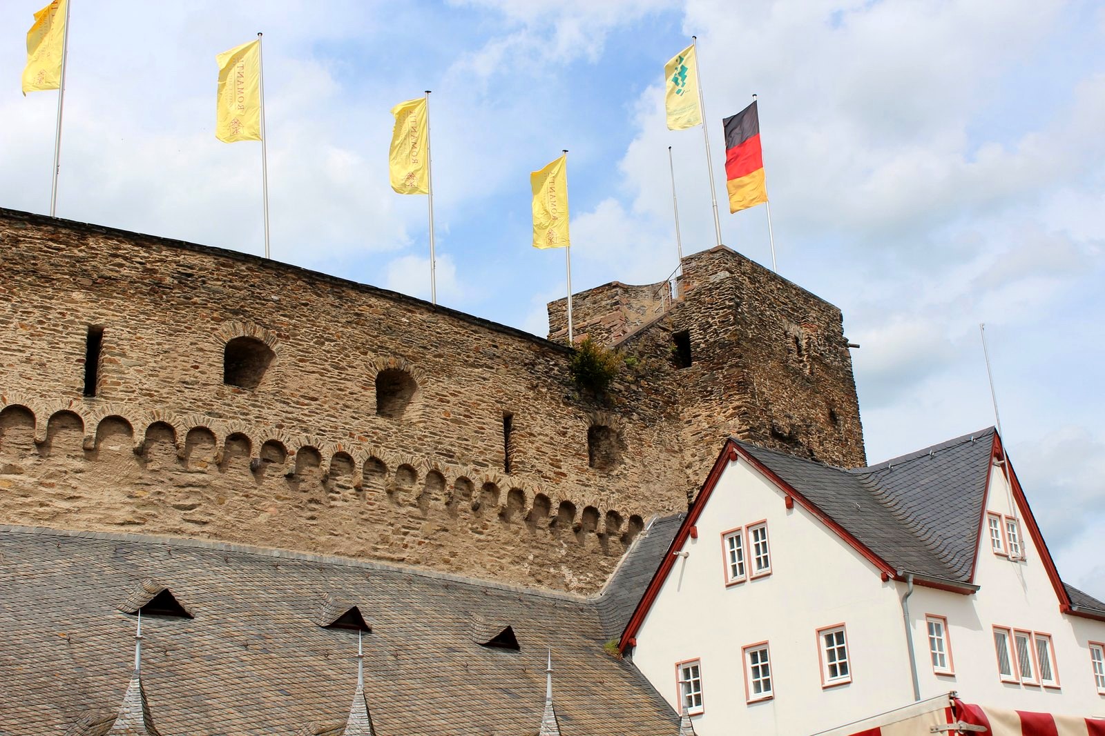 Muralha arredondada de Burg Rheinfels com bandeiras no topo e o hotel ao lado