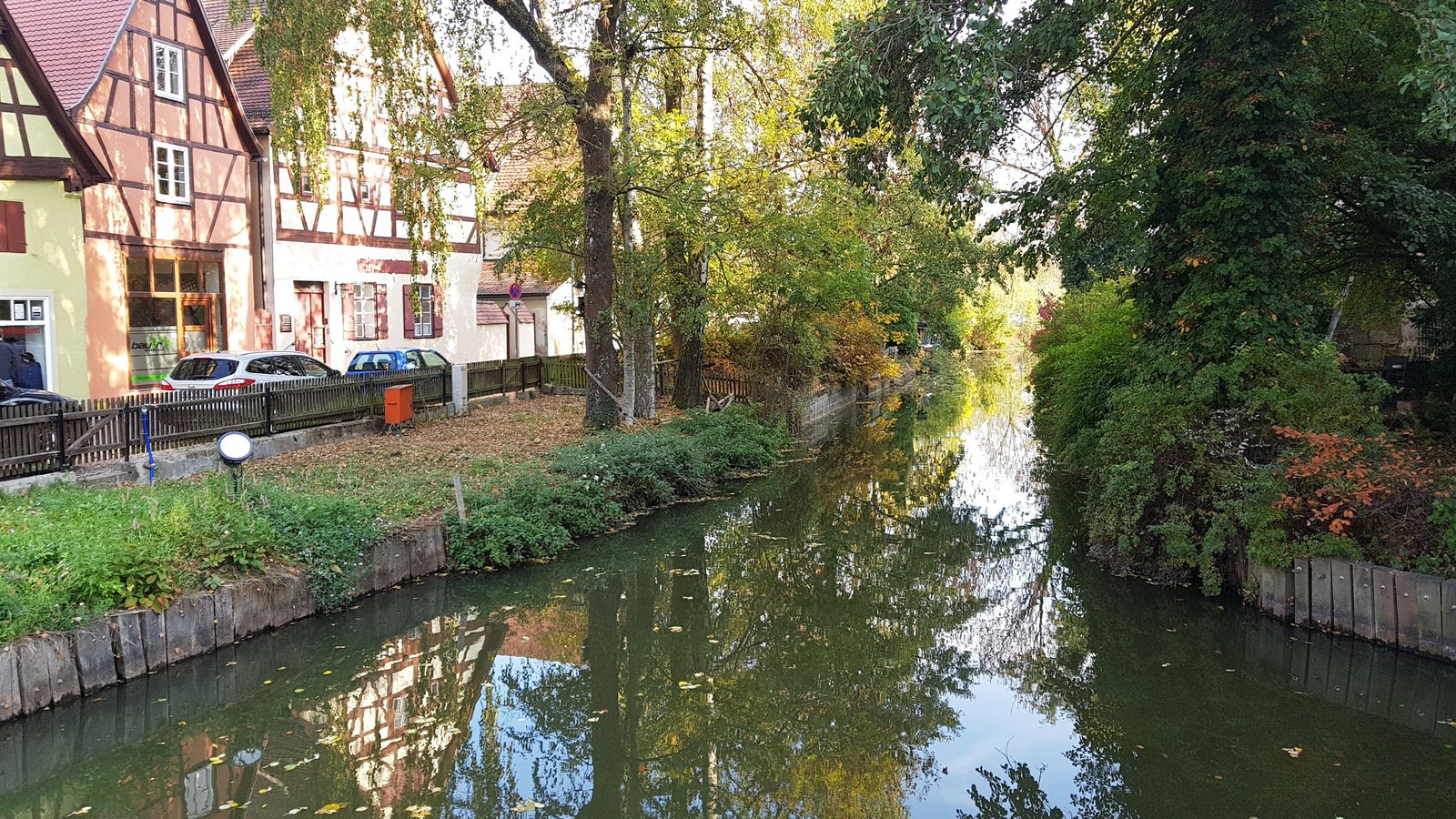 Casas de enxaimel à beira do canal em Dinkelsbühl, com árvores em cores de outono