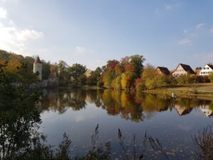 Muralha e torre de Dinkelsbühl refletidas no lago do fosso, cercadas por árvores de outono