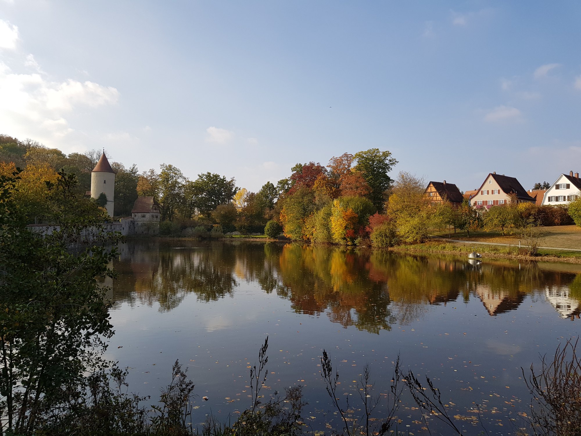 Muralha e torre de Dinkelsbühl refletidas no lago do fosso, cercadas por árvores de outono