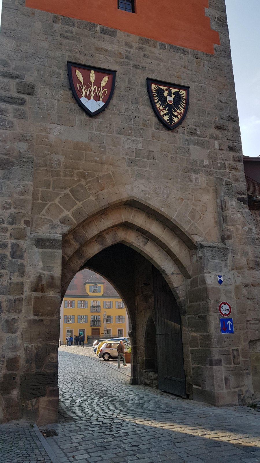 Arco gótico do portão de Dinkelsbühl com brasões, visto da rua de paralelepípedos