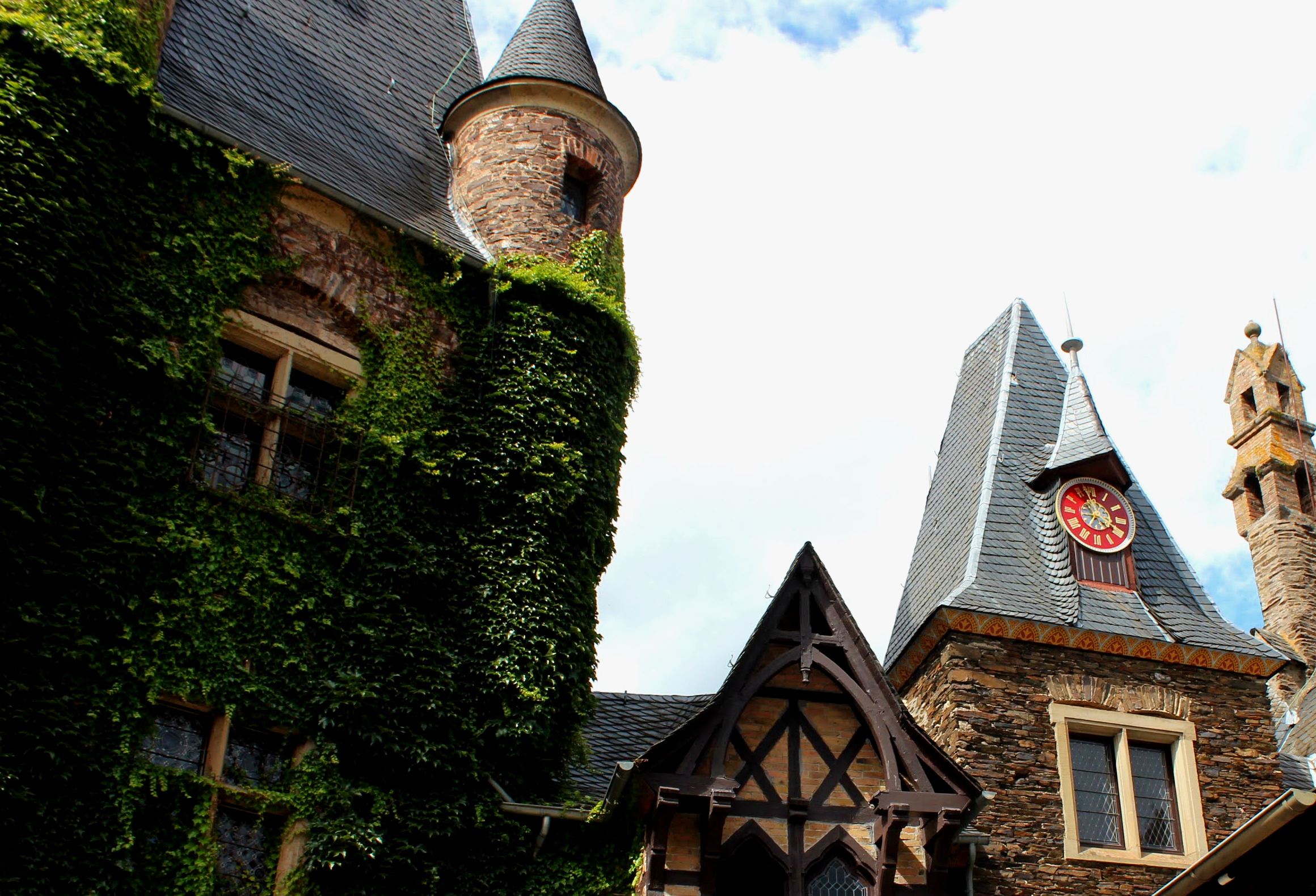 Pátio interno do Reichsburg de Cochem com parede coberta de hera, torreão de ardósia, torre do relógio e frontão de enxaimel