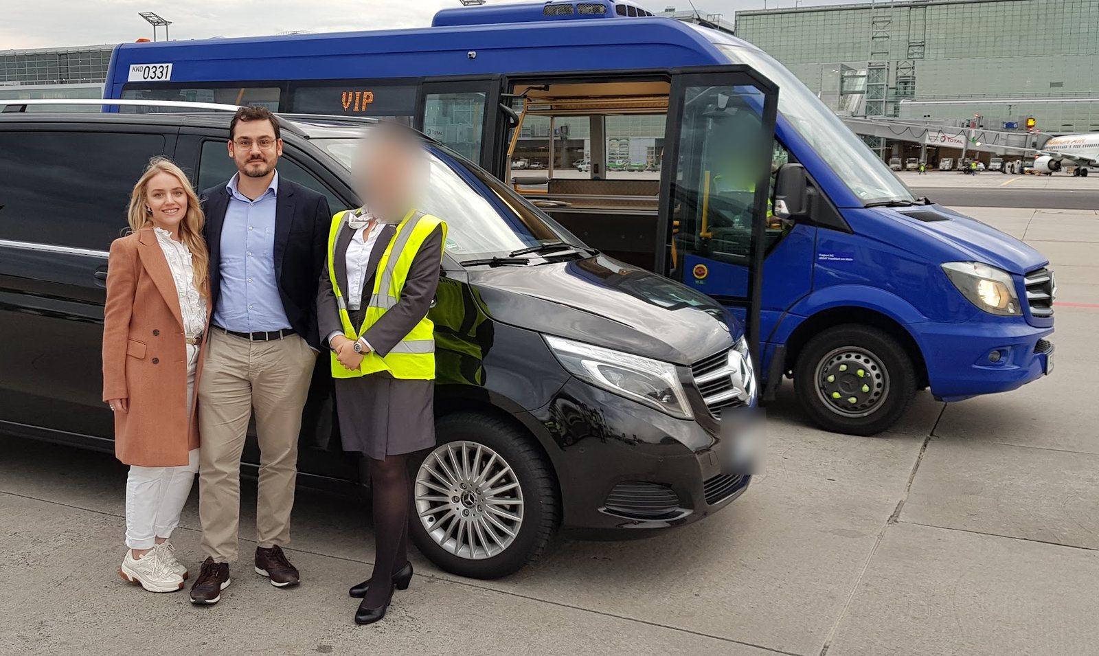 Rafaella e Raphael, da Viagem Alemanha, com uma funcionária do serviço VIP na pista do aeroporto de Frankfurt, diante de uma van preta e do ônibus VIP azul