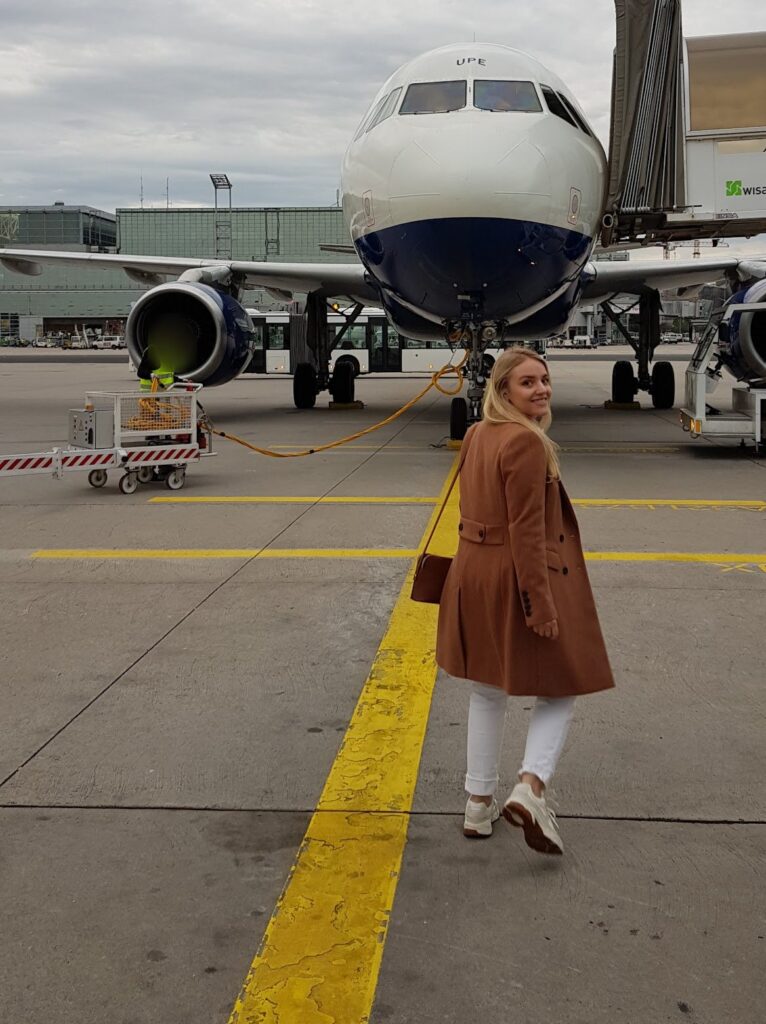 Rafaella Vilafranca, da Viagem Alemanha, olha para trás enquanto caminha pela pista do aeroporto de Frankfurt em direção a um avião estacionado