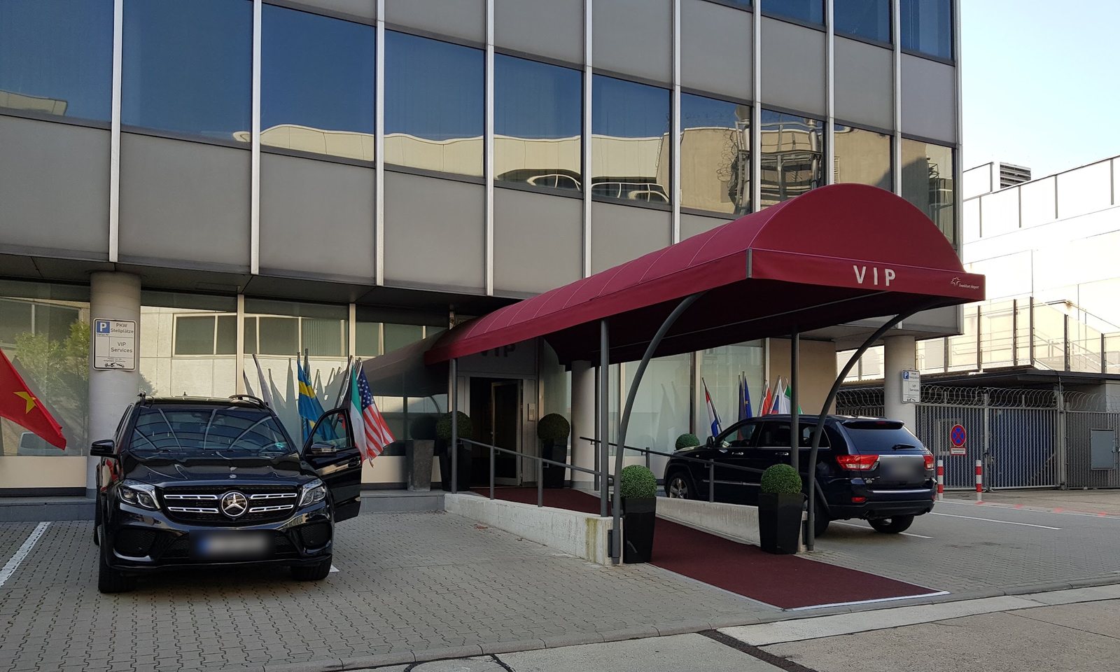 Entrada do antigo terminal VIP do aeroporto de Frankfurt em 2019, com toldo vermelho, tapete e um veículo executivo preto estacionado