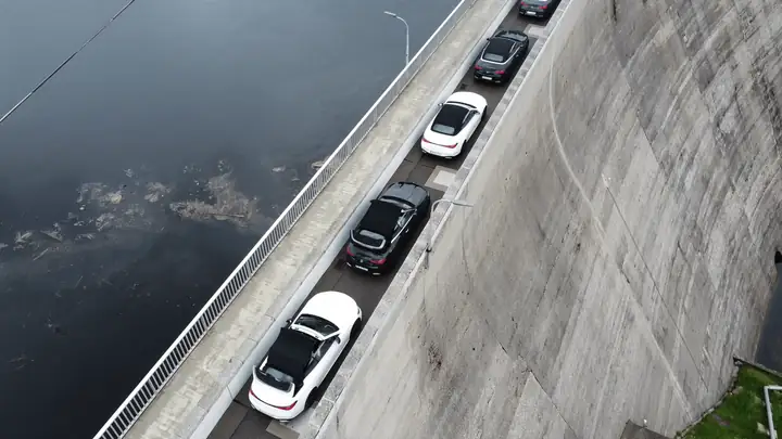 Comboio de conversíveis do Cabrio Tour atravessando uma represa, vista aérea