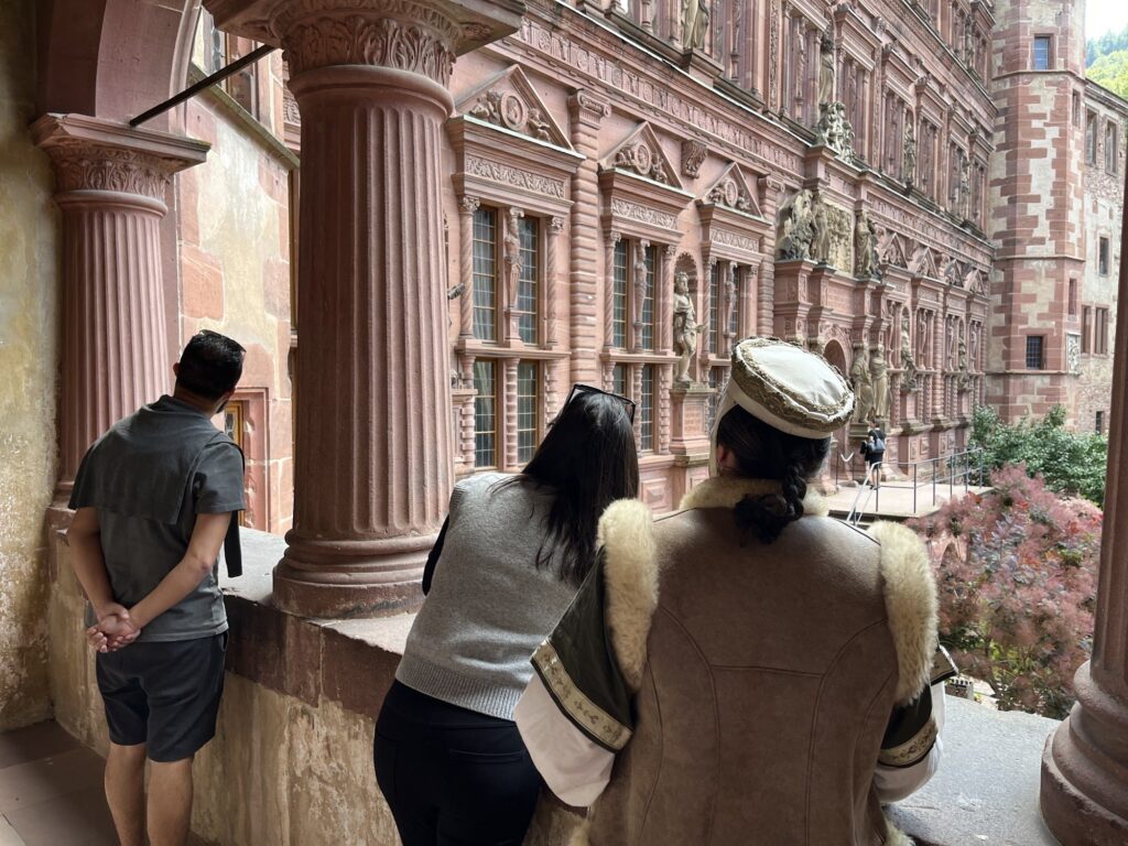 Viajantes e um guia caracterizado nas arcadas do Salão de Vidro, de frente para o Ottheinrichsbau