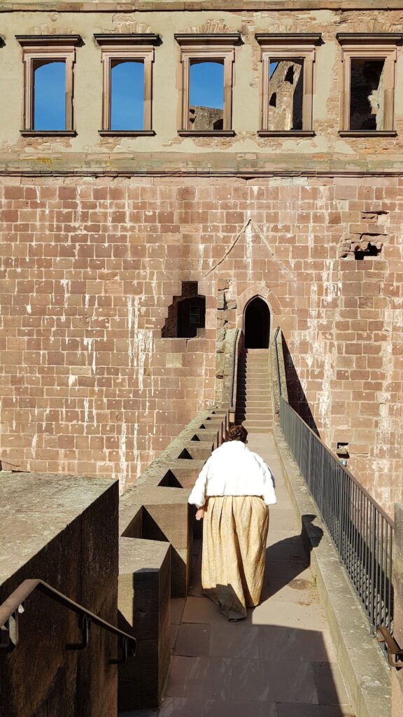 Guia com traje de época subindo uma escada estreita de pedra no Castelo de Heidelberg