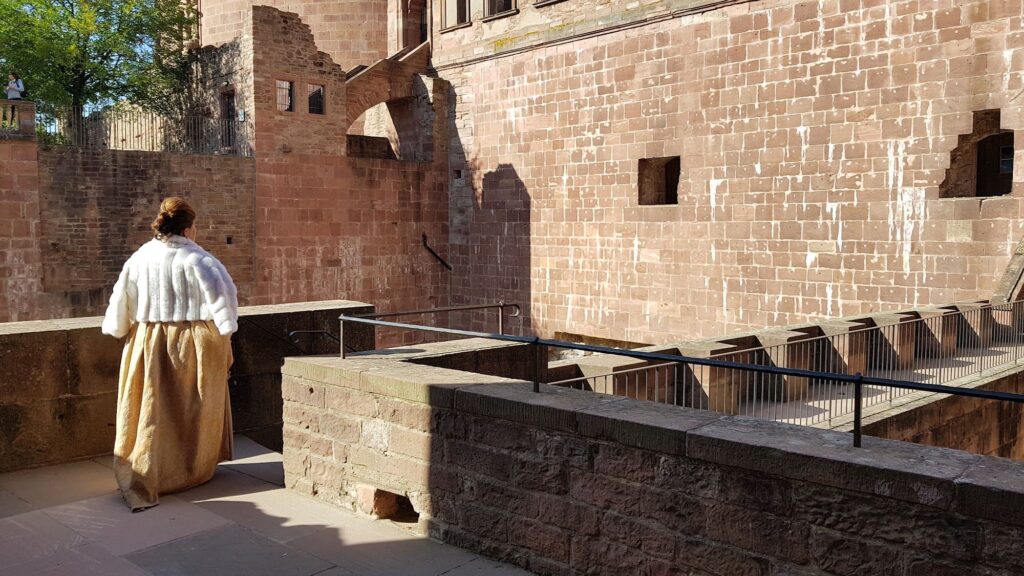 Guia com traje de época caminhando pelas muralhas de arenito vermelho do Castelo de Heidelberg