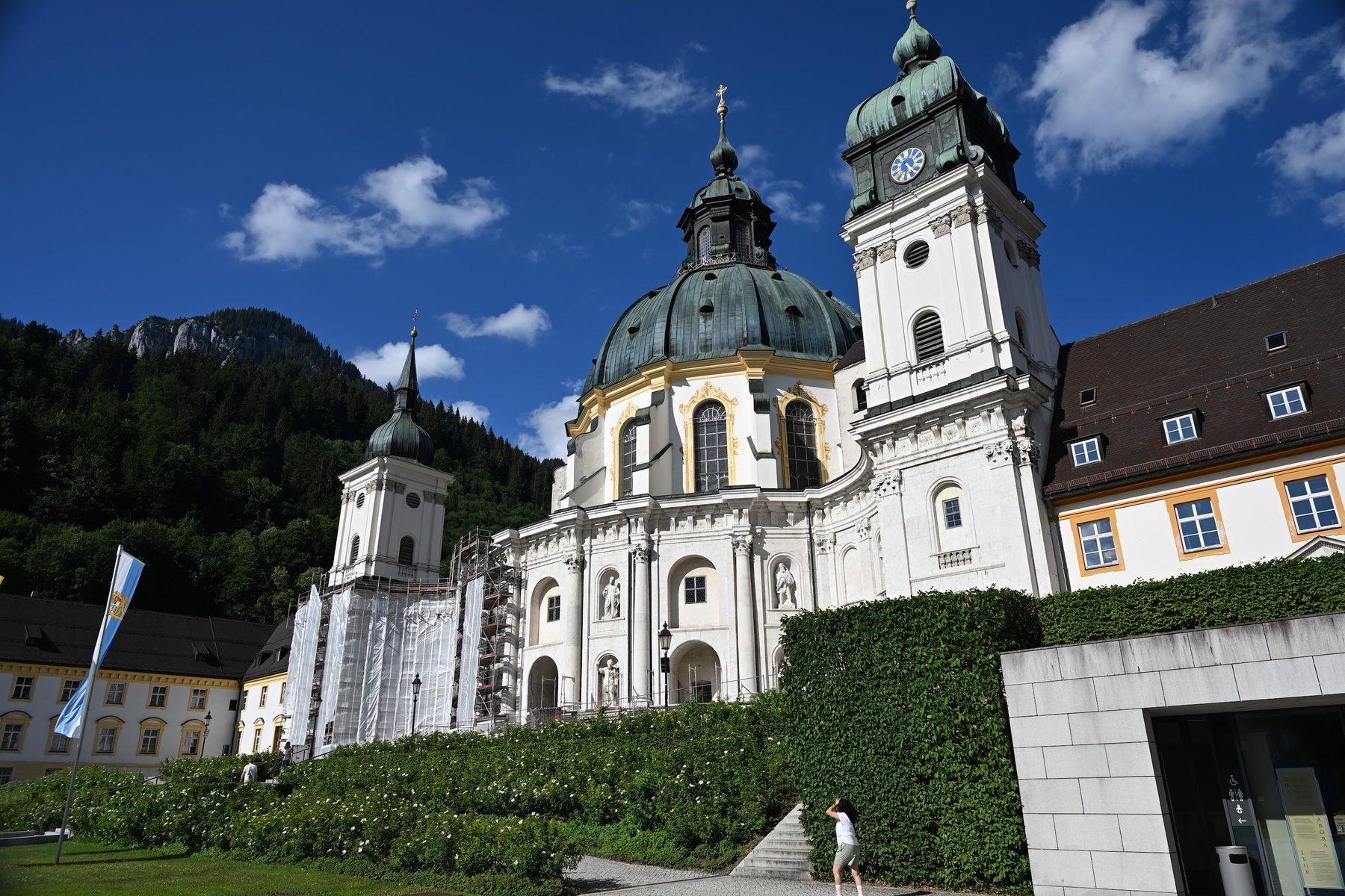 Fachada do Mosteiro de Ettal com a cúpula de cobre e a torre do relógio, e a montanha dos Alpes de Ammergau ao fundo