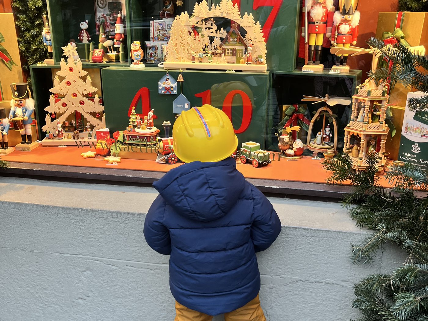 Criança de costas diante de uma vitrine de decoração natalina alemã, com pirâmides de madeira e quebra-nozes