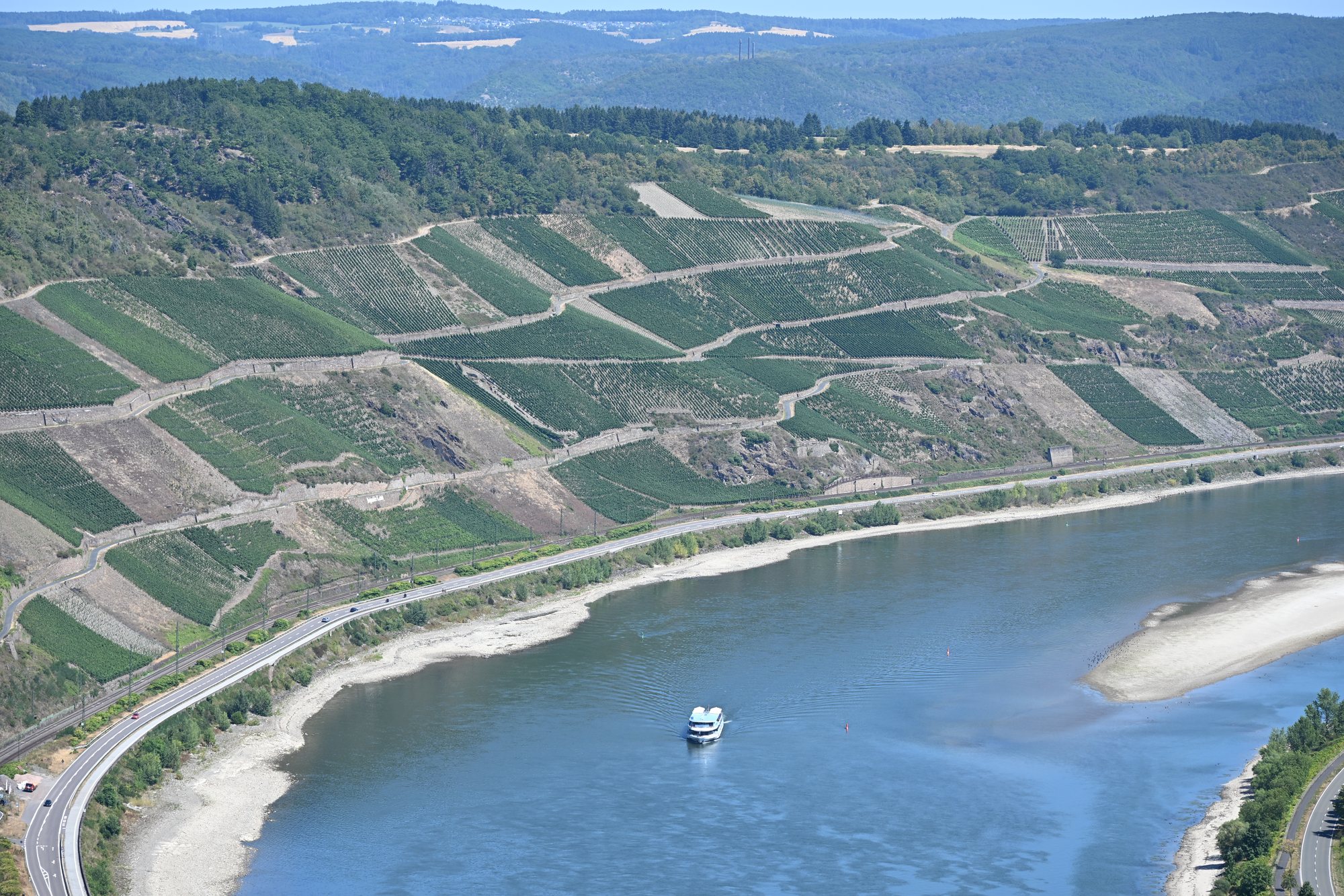 O Bopparder Hamm visto do Gedeonseck: curva do Reno com vinhedos em socalcos, estrada e ferrovia junto à margem e um barco de passeio no rio