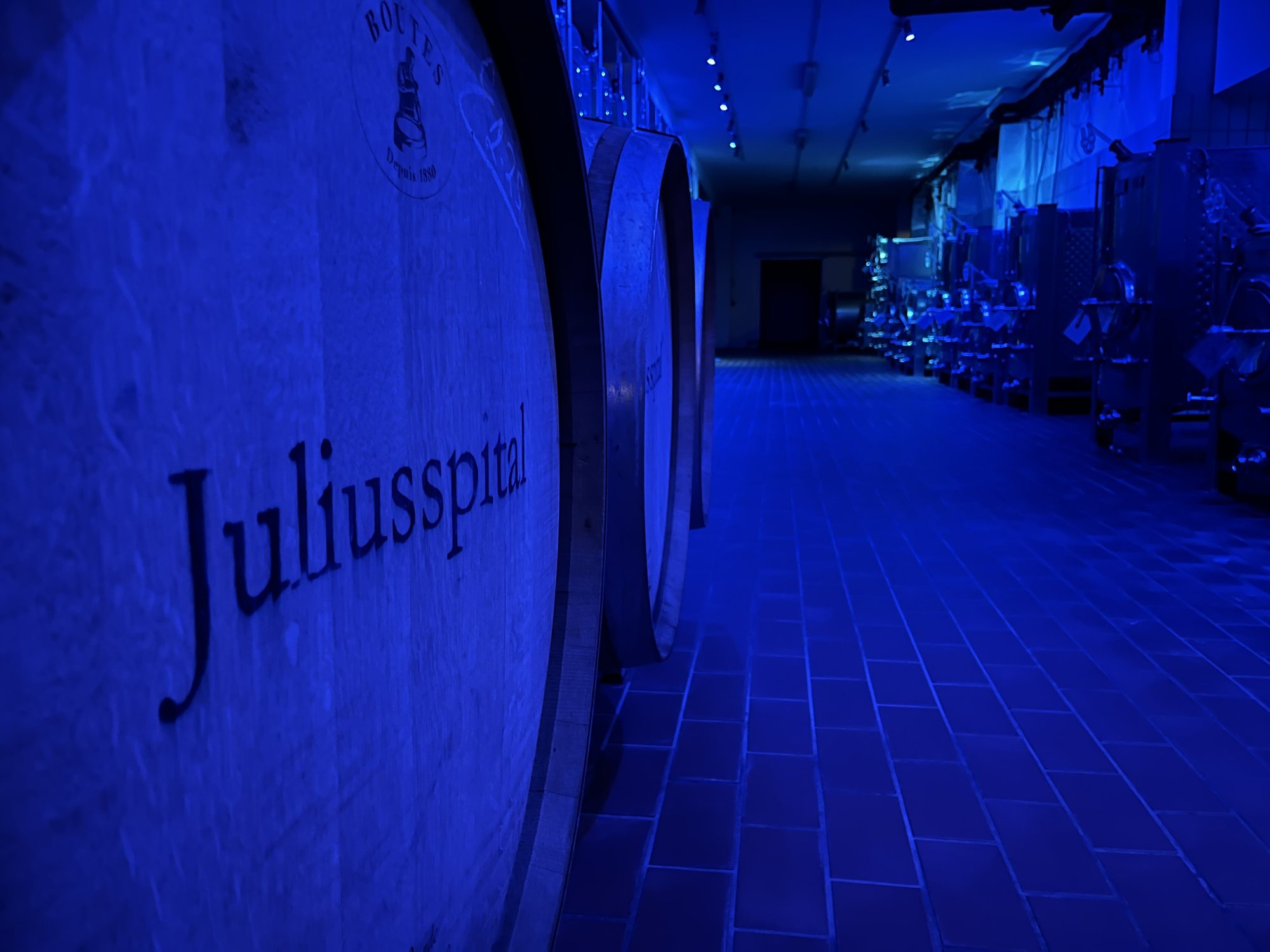 Barril com o nome Juliusspital em primeiro plano, numa adega iluminada em azul, em Würzburg