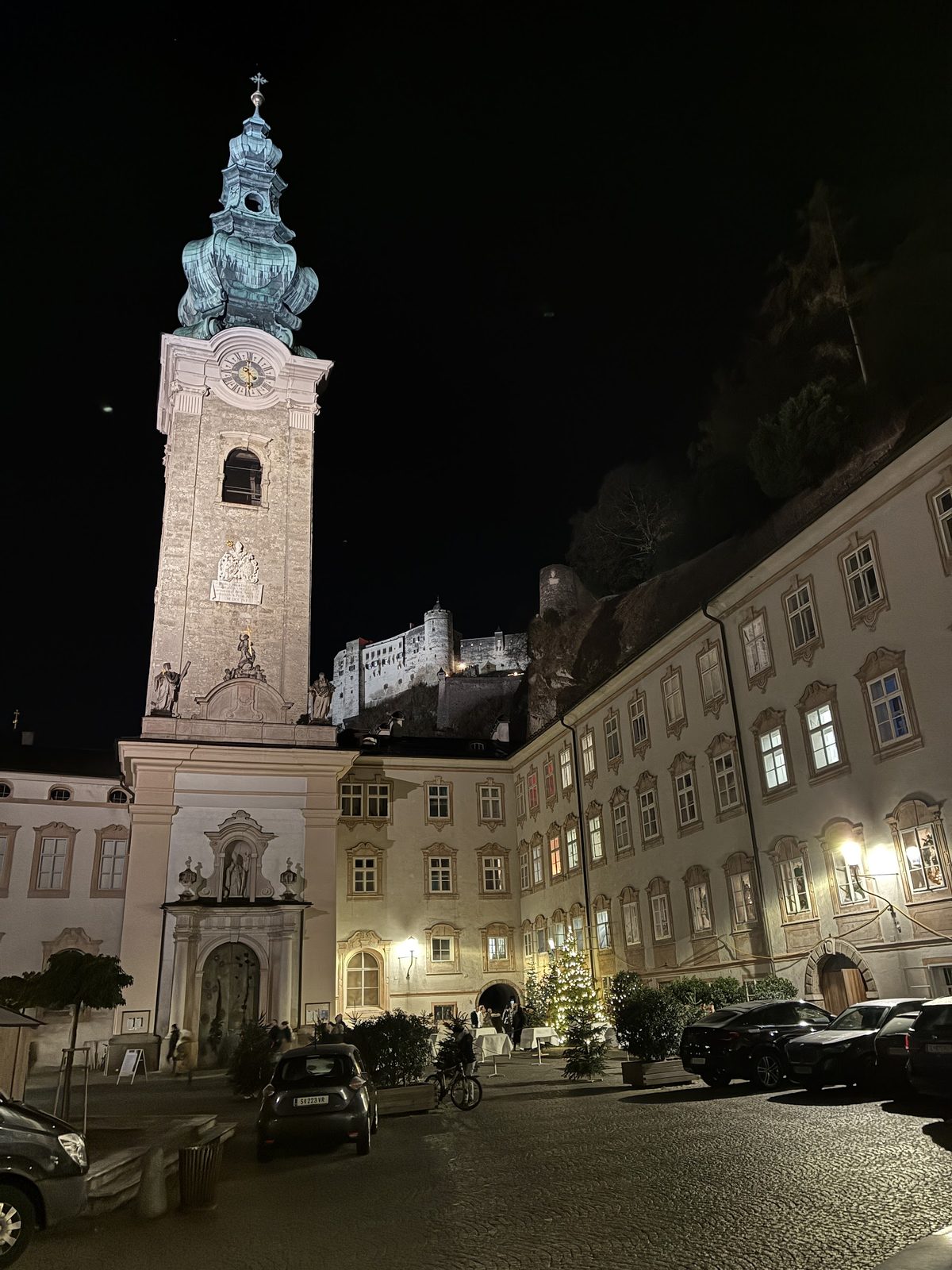Torre e pátio da Abadia de St. Peter iluminados à noite, com a Fortaleza Hohensalzburg acesa no alto