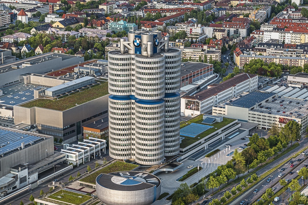 Vista aérea da sede da BMW em forma de quatro cilindros, do Museu da BMW em forma de tigela com o logotipo no telhado e dos prédios da fábrica ao redor, em Munique