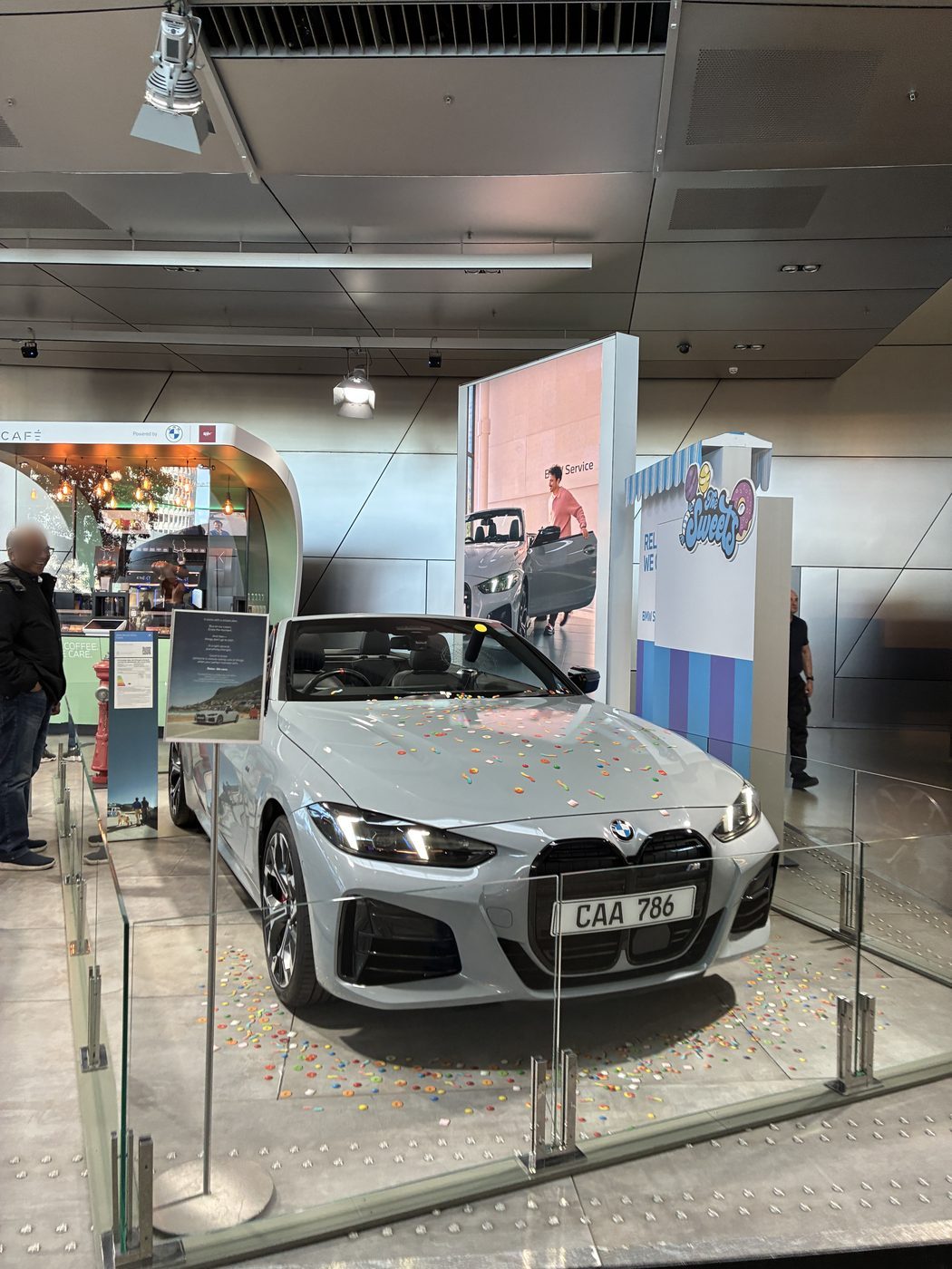 BMW conversível cinza em exposição no BMW Welt, cercado por vidro, com confetes coloridos no piso