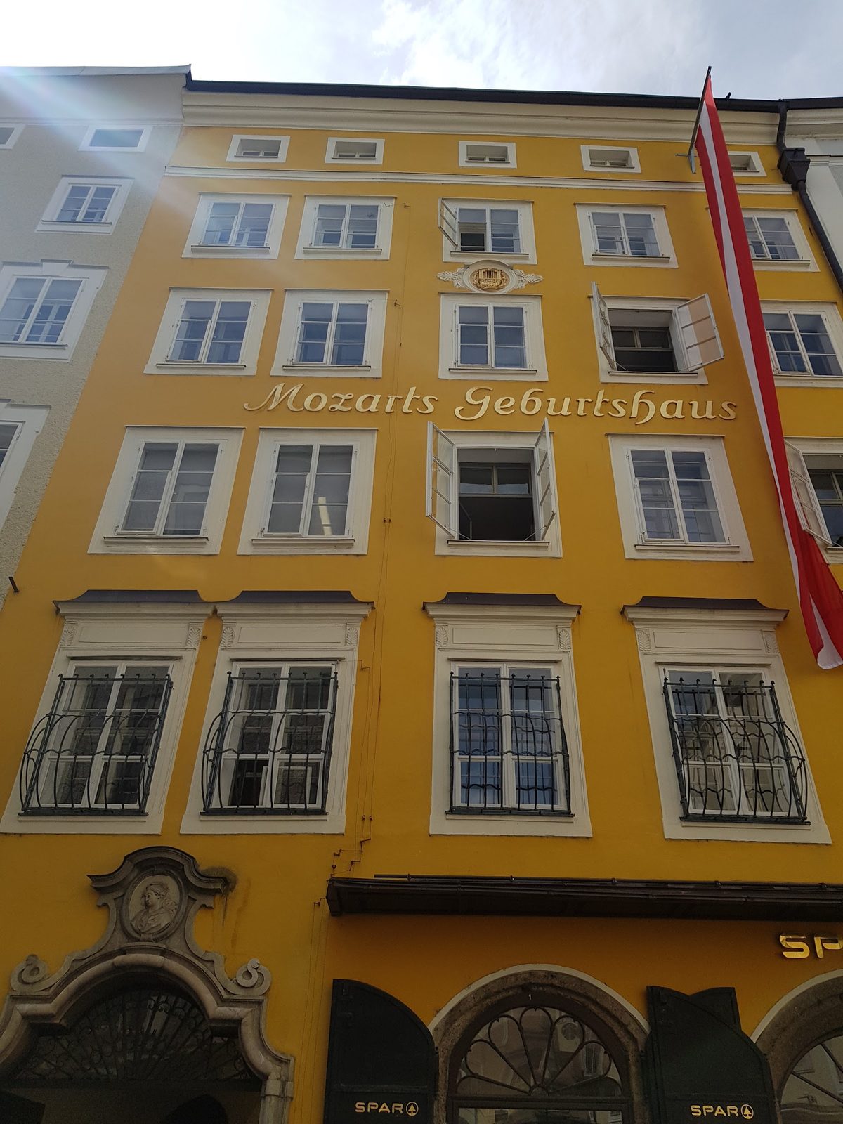 Fachada amarela da Casa Natal de Mozart, na Getreidegasse, com a inscrição Mozarts Geburtshaus e a bandeira da Áustria