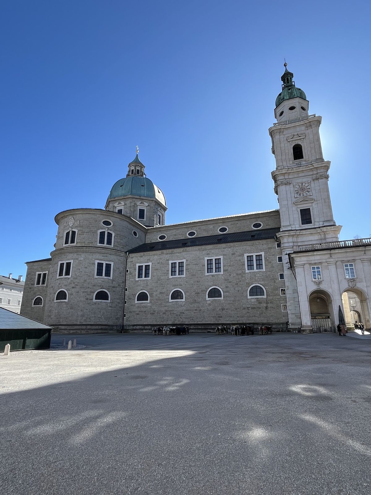 A Catedral de Salzburgo vista de fora, com a cúpula verde, uma das torres brancas e as paredes de pedra clara, sob céu azul