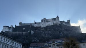 A Fortaleza Hohensalzburg, branca, no alto do rochedo escuro do Festungsberg, vista de uma praça da Cidade Velha de Salzburgo num dia de inverno