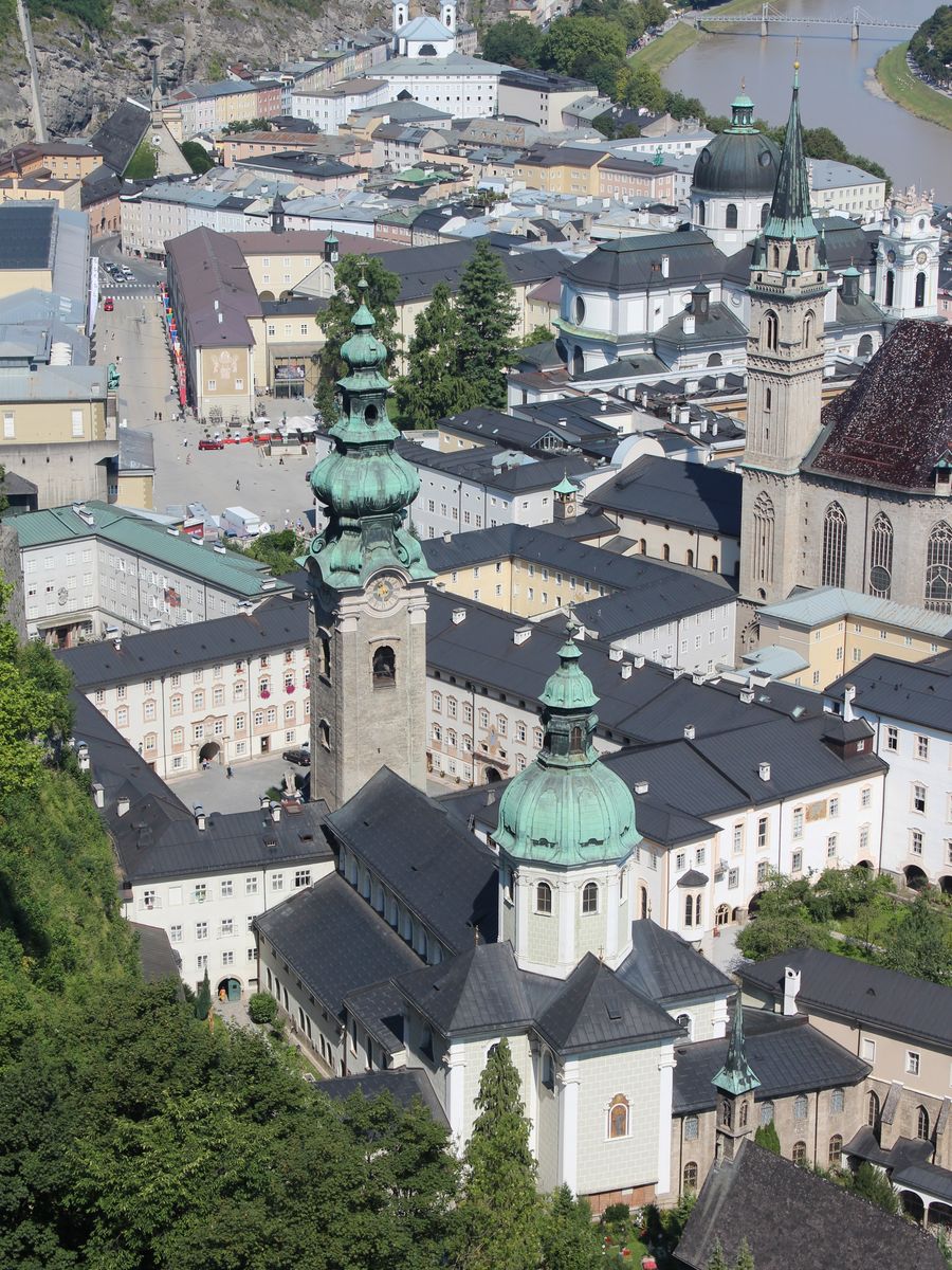 Vista do alto da fortaleza sobre as cúpulas verdes de St. Peter, a torre pontuda da igreja dos Franciscanos, os telhados da Cidade Velha e o rio Salzach ao fundo