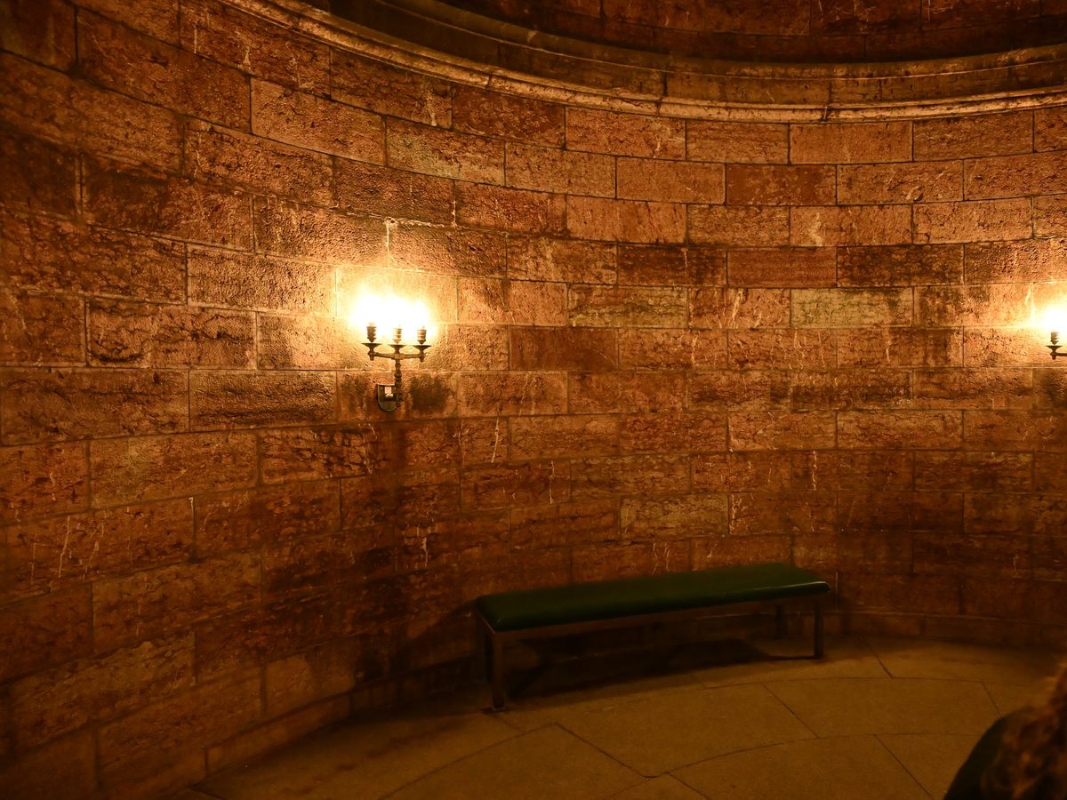 Sala circular de pedra com arandelas acesas e um banco verde, no fim do túnel do Kehlsteinhaus