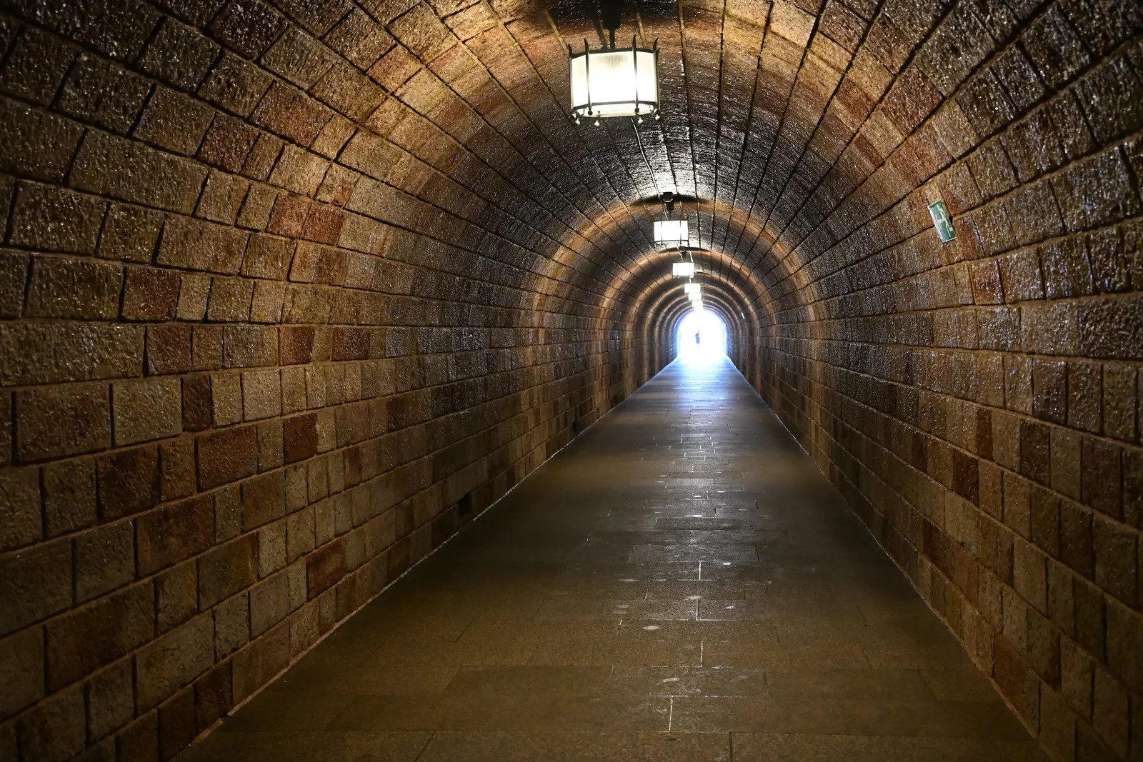 Túnel comprido de blocos de pedra, iluminado por luminárias no teto, que leva ao elevador do Kehlsteinhaus