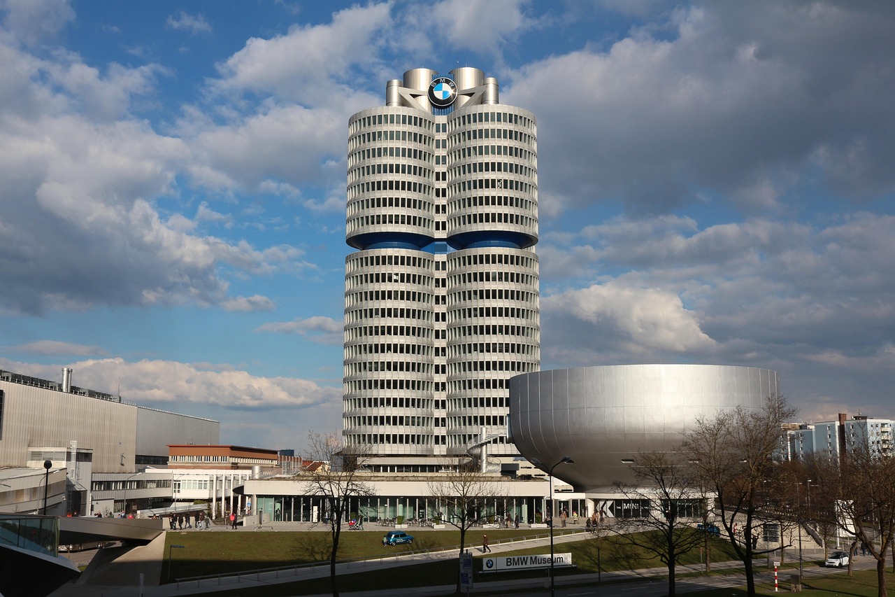 Sede da BMW em forma de quatro cilindros ao lado do prédio prateado em forma de tigela do Museu da BMW, em Munique, sob céu azul com nuvens