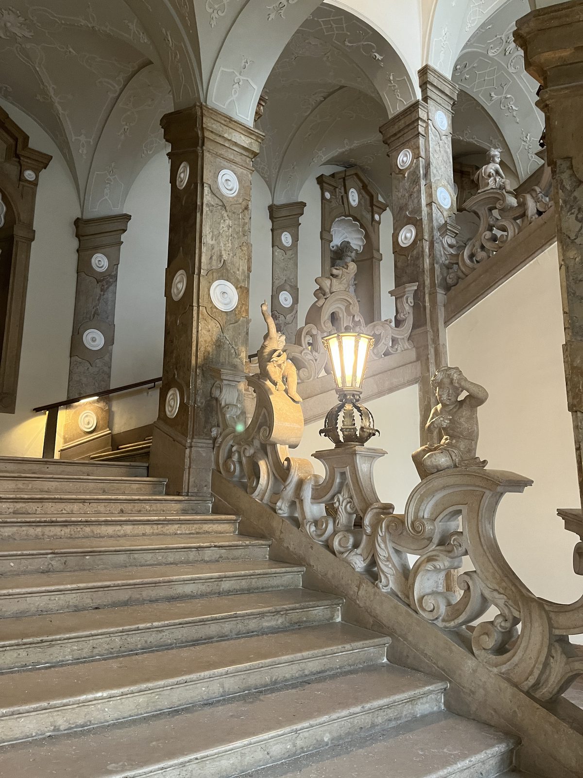 Escadaria barroca do Palácio Mirabell com balaustrada de mármore branco decorada com anjinhos esculpidos e uma lanterna de ferro
