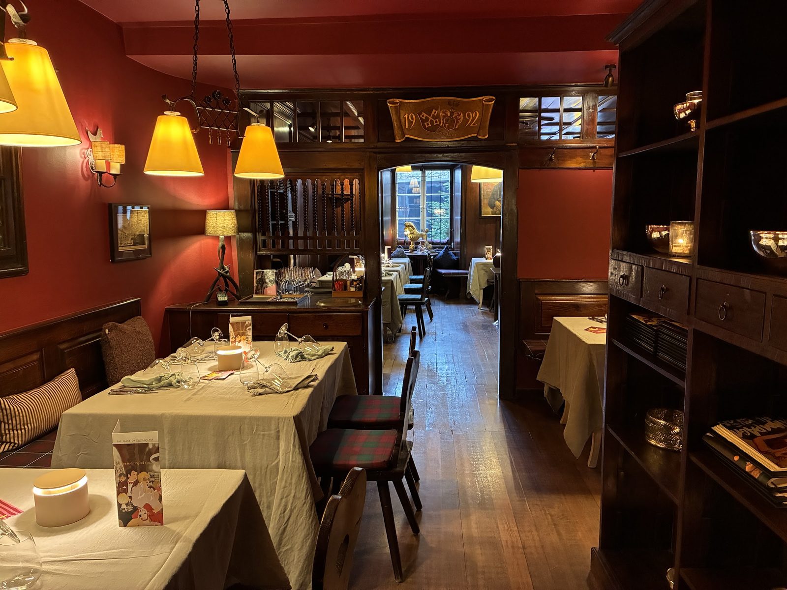 Salão do restaurante St. Peter Stiftskulinarium com paredes vermelhas, luminárias amarelas, mesas postas e móveis de madeira escura
