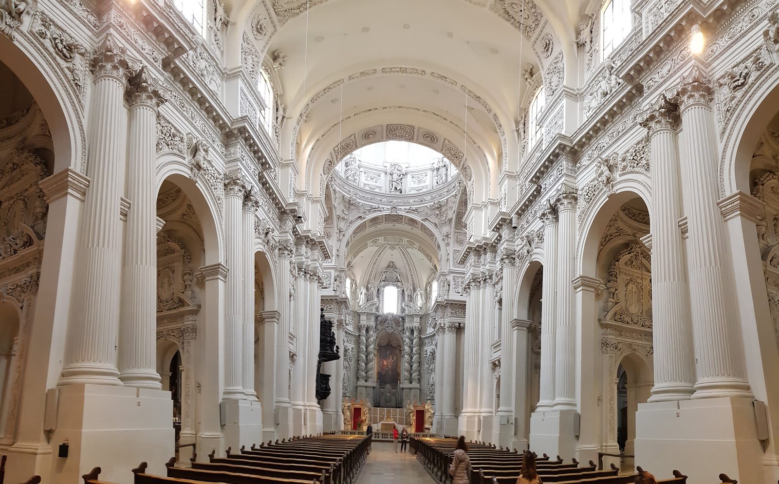 Interior branco da Theatinerkirche, em Munique, com colunas, arcos decorados em estuque e a cúpula ao fundo