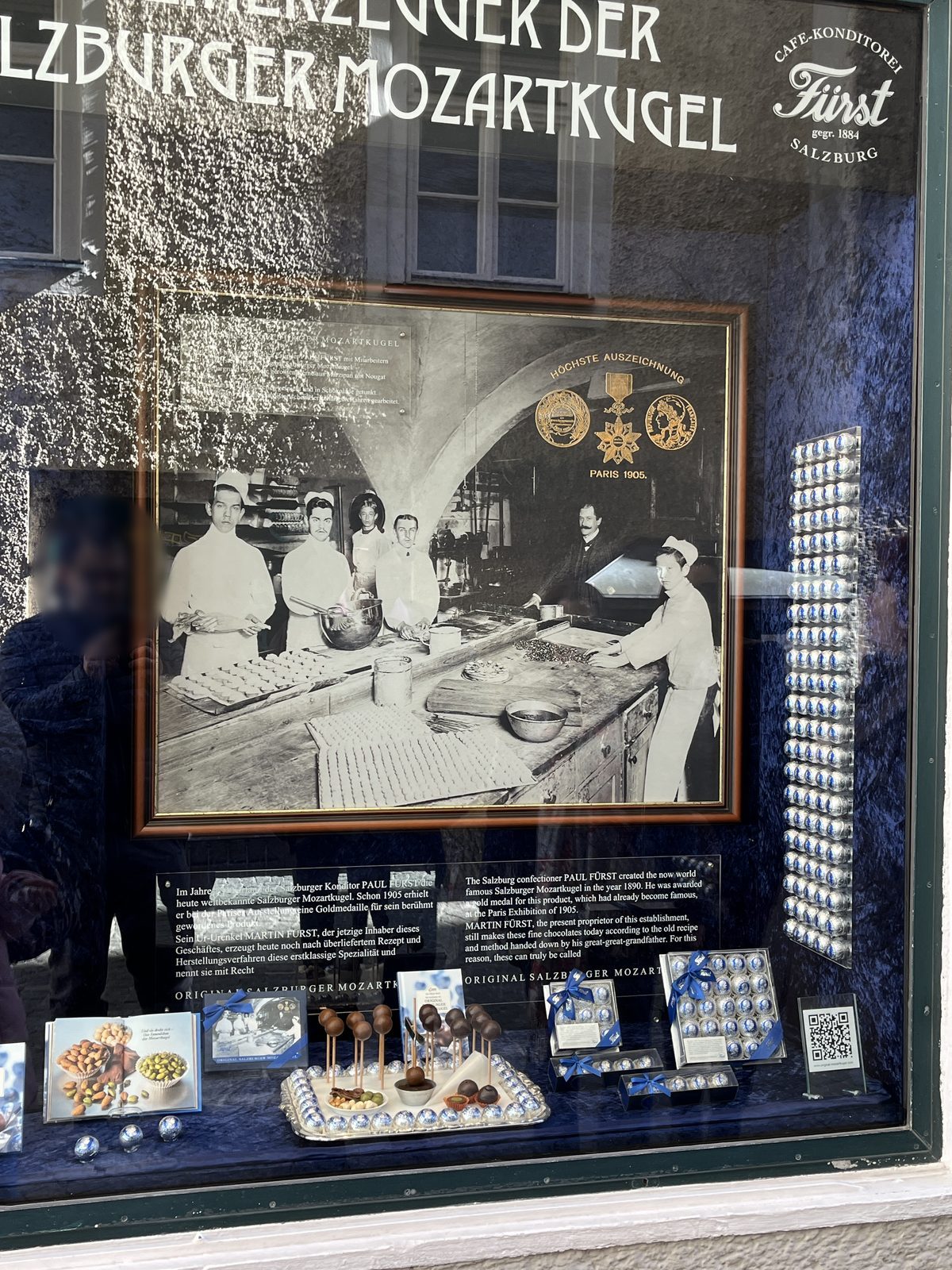 Vitrine da Café-Konditorei Fürst em Salzburgo, com uma foto antiga dos confeiteiros, medalhas e Mozartkugeln embrulhadas em papel prateado e azul