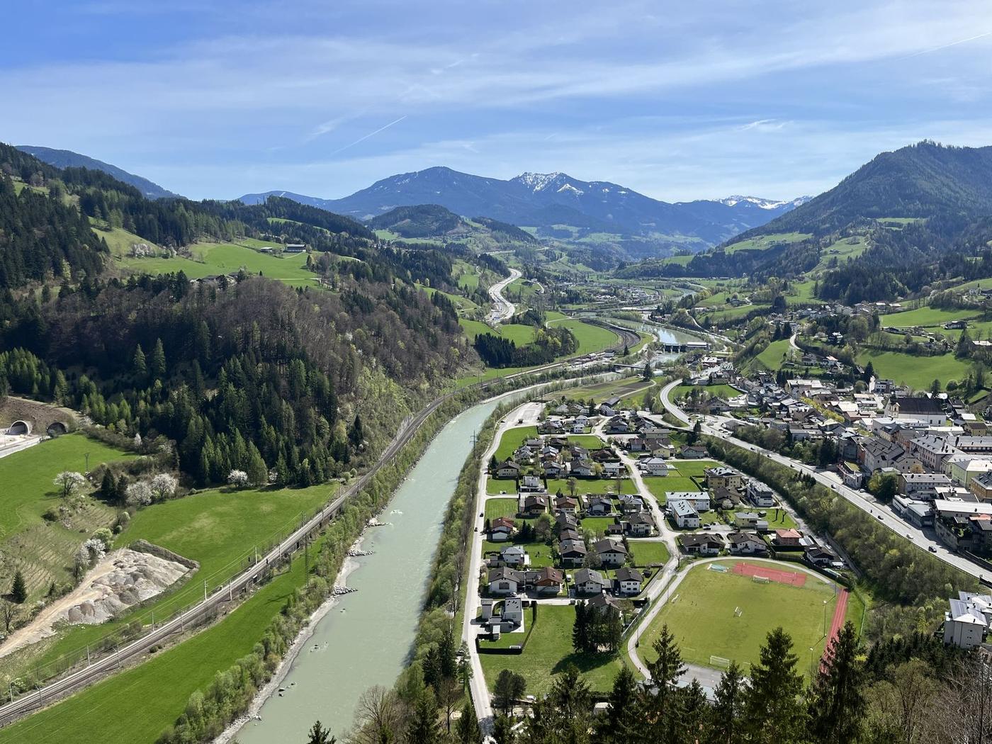 Vista do alto do castelo sobre o vale do Salzach, com o rio verde-claro, casas de Werfen, um campo de futebol e montanhas cobertas de floresta