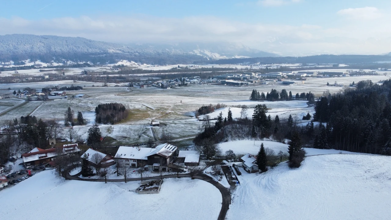 Paisagem rural do Allgäu com telhados, árvores e faixas de neve sobre os campos