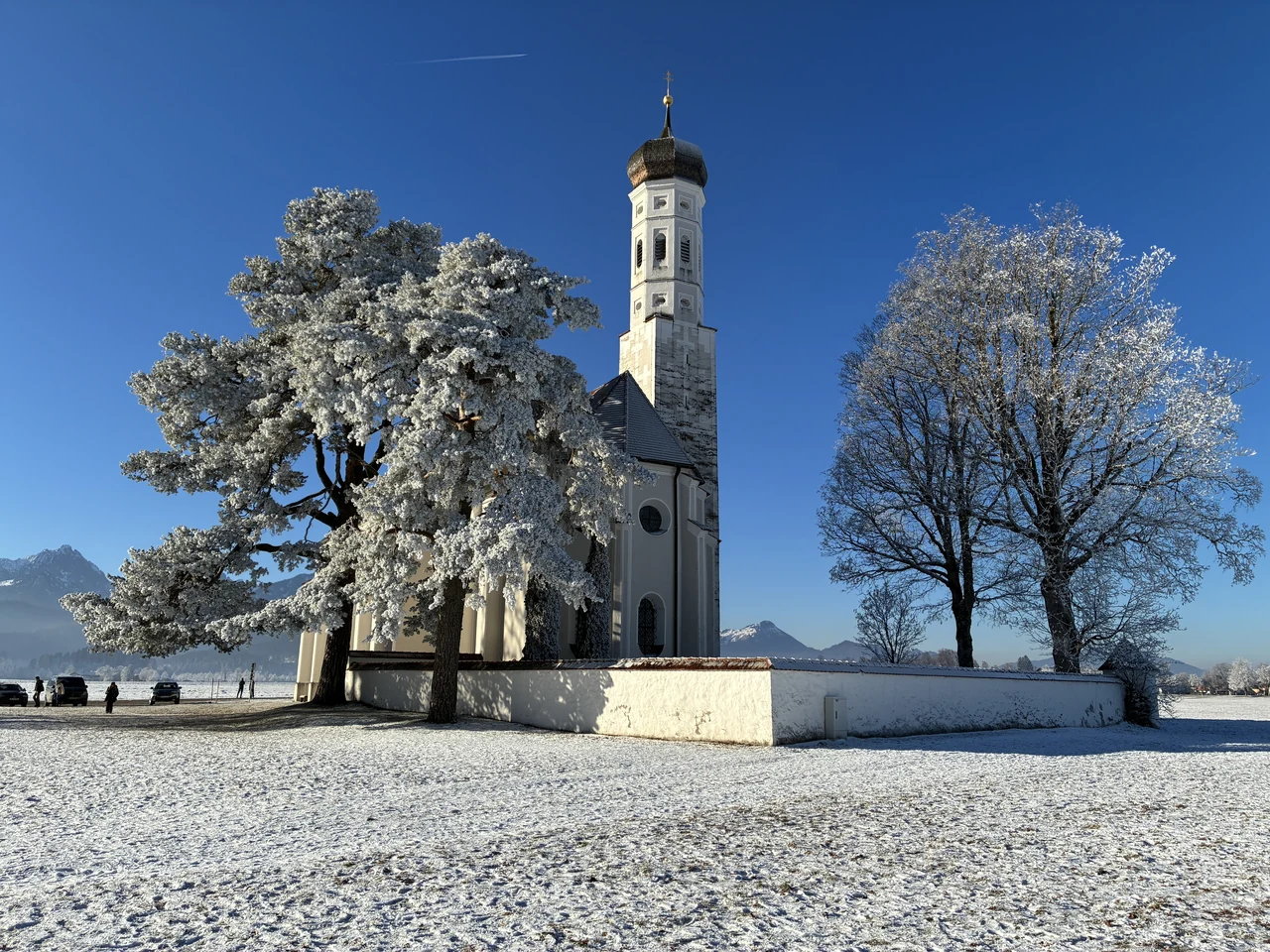 Igreja de St. Coloman junto a árvores brancas de geada e um campo com neve