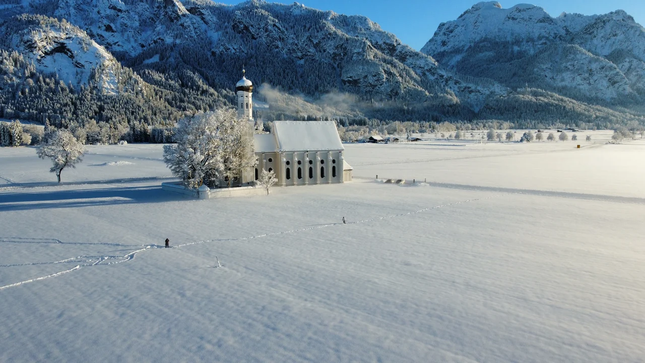 Igreja de St. Coloman e campos cobertos de neve diante das montanhas de Schwangau