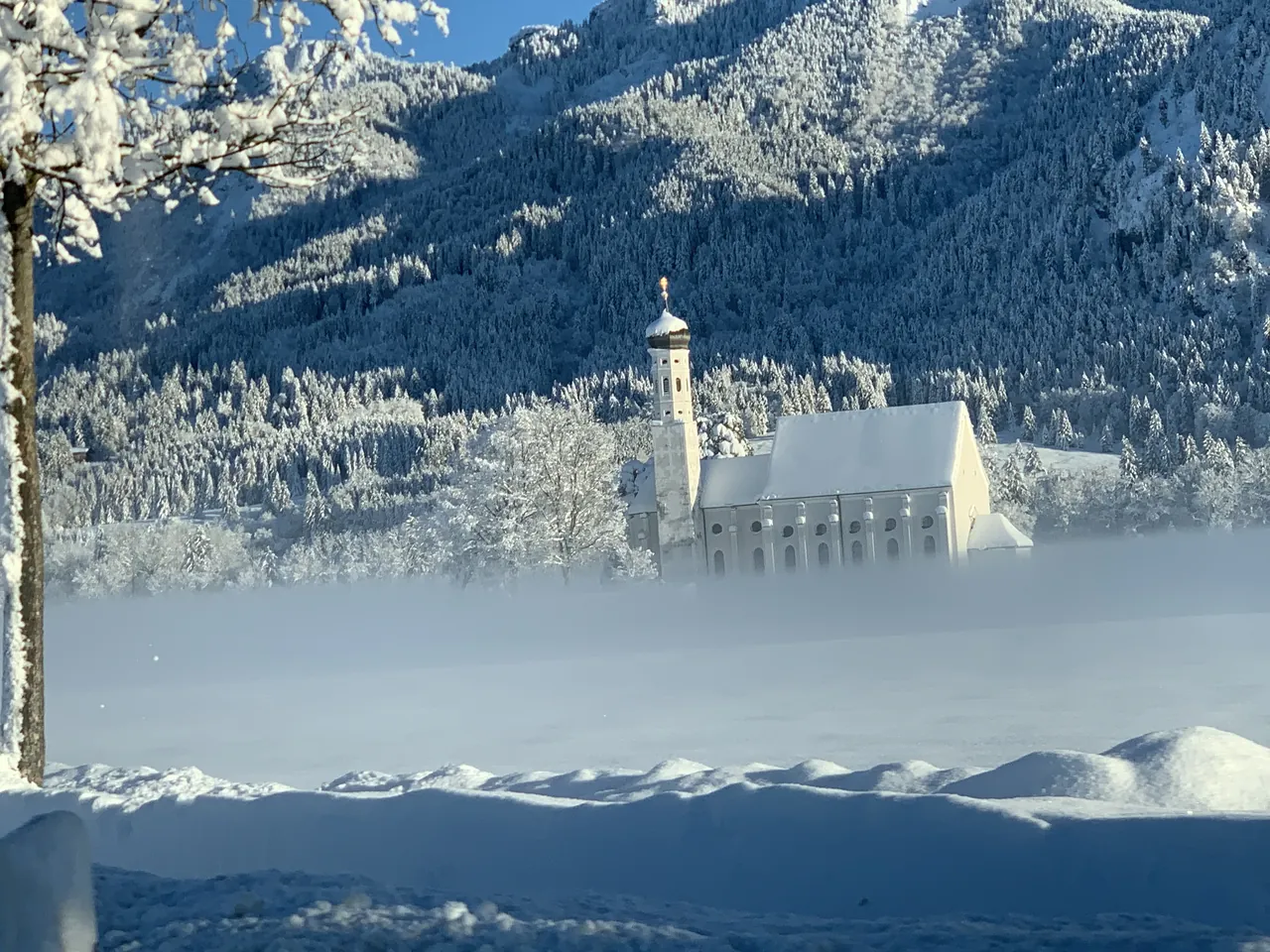 Igreja de St. Coloman cercada de neve e árvores brancas diante das montanhas de Schwangau