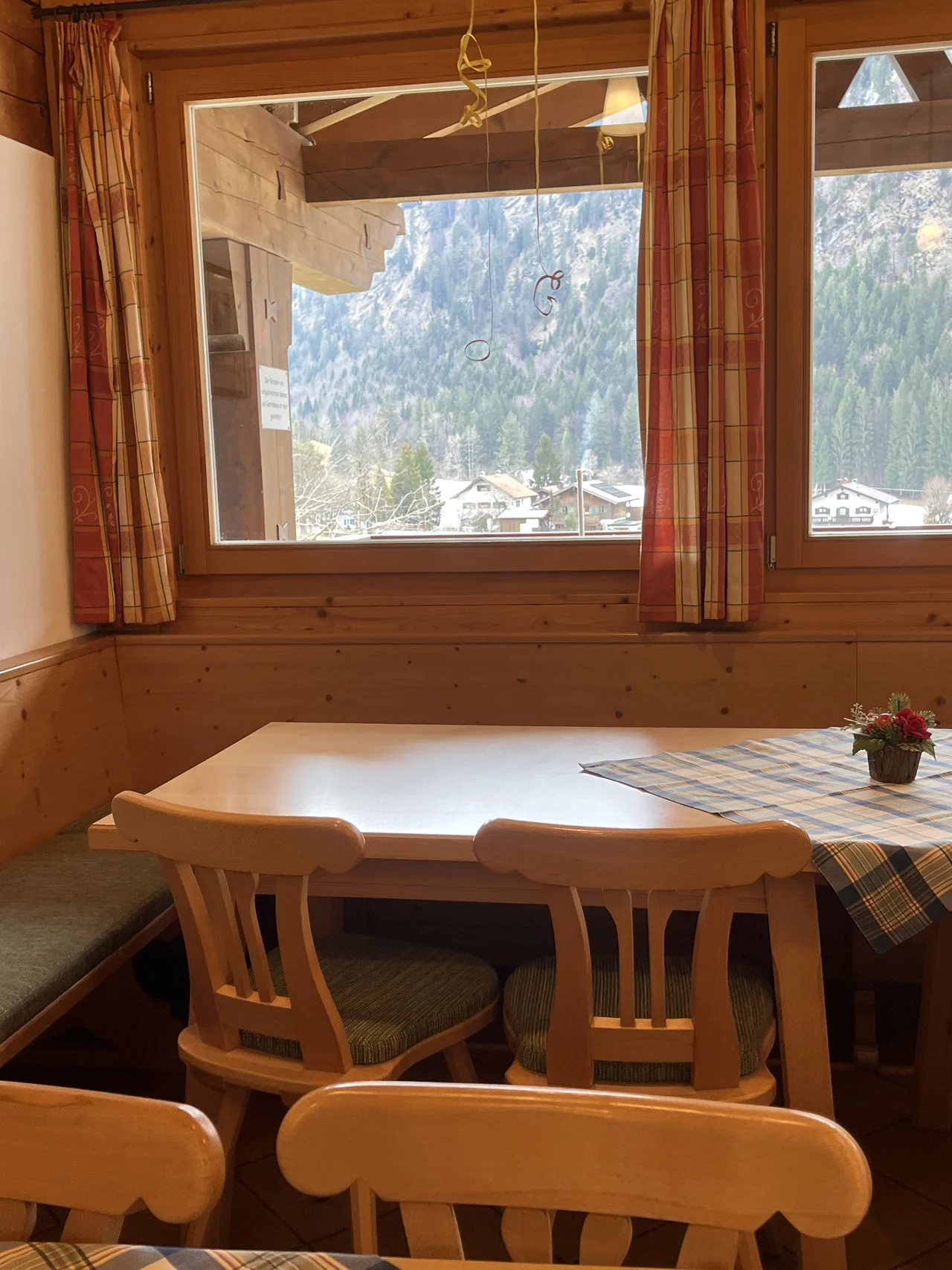 Mesa e cadeiras de madeira junto à janela de um restaurante, com vista para montanhas em Ettal