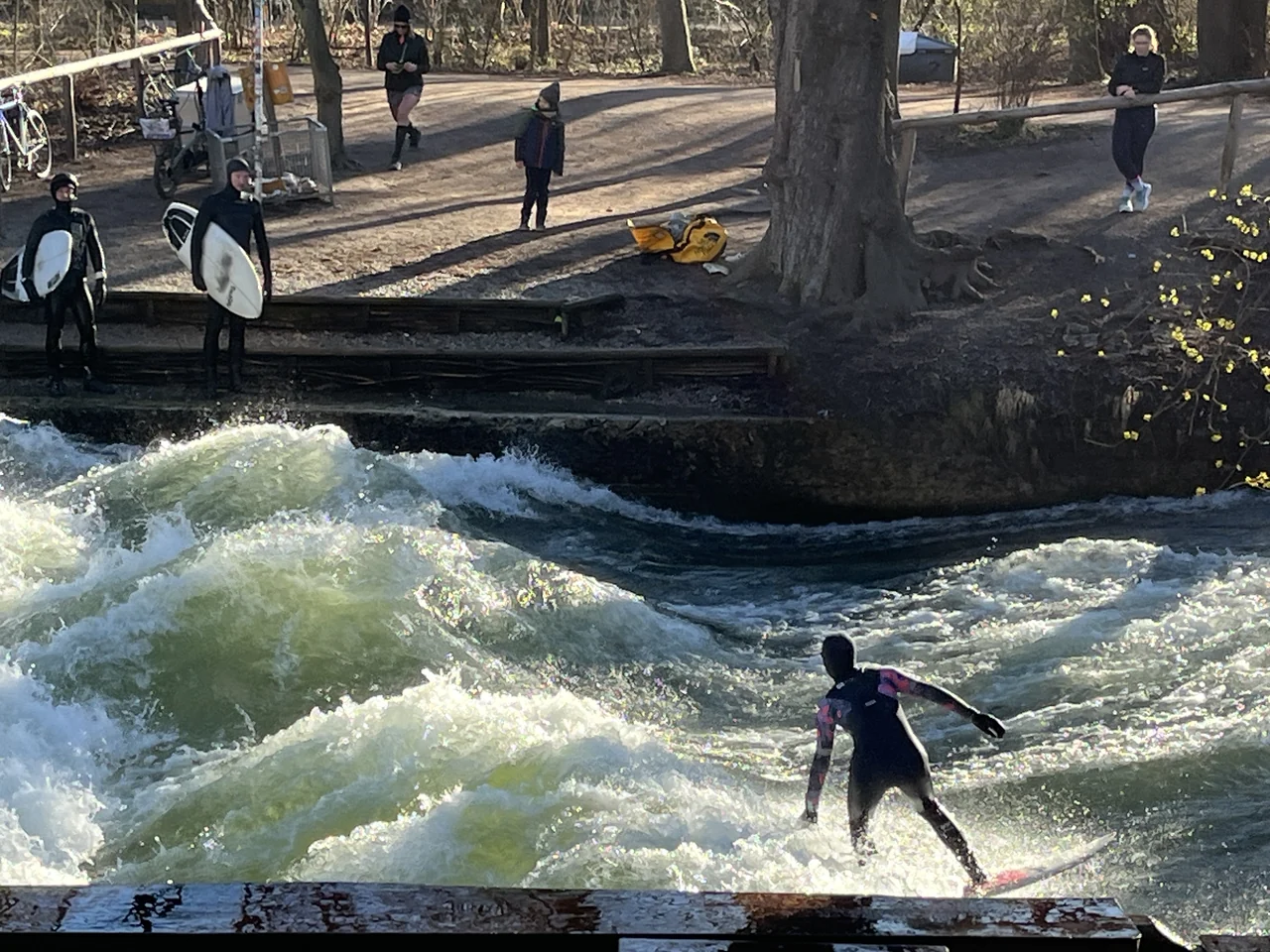 Surfista sobre uma onda no Eisbach, em Munique, com pessoas observando da margem